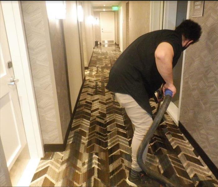 Water damage technician extracting water from a hotel hallway.