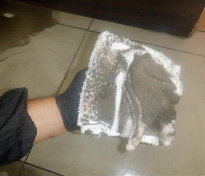 A hand holding a white towel filled with soot and ash from a recent fire in a home.