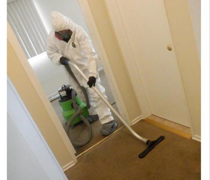A water damage technician in a PPE suit with a wand in hand extracting water from a carpet.