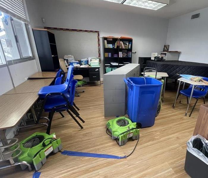 Air movers placed in a classroom, blowing air to dry after water damage. The room is equipped with several fans